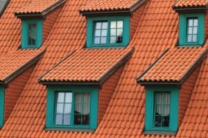 Close-up of a sloped roof with orange tiles, featuring several green-trimmed dormer windows—craftsmanship you’d expect from an expert roofing company.