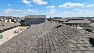 View of a residential neighborhood showing the shingled roof of a house in the foreground, with several other houses under a blue sky with clouds—ideal for assessing Roof Replacement Cost Dallas TX.
