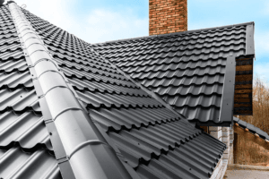 Close-up view of a house roof covered with dark gray metal roofing sheets and a brick chimney under a blue sky, showcasing quality roofing services and excellent roof replacement value.