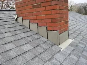 Brick chimney with step flashing installed along its base on an asphalt shingle roof, clearly displaying proper overlap for water protection—a great example from a comprehensive roof flashing guide.