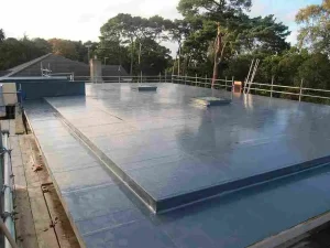 A flat roof with a grey, reflective waterproof covering—highlighting quality flat roof materials type—is surrounded by safety railings and trees in the background.