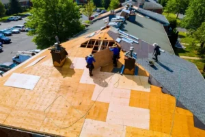 Three workers are installing new plywood sheets on a sloped roof, with shingles and materials nearby—a typical scene when assessing roof replacement cost in San Antonio.