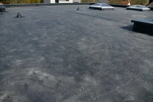 Flat roof covered with a smooth, dark rubber membrane, featuring a few vents and a skylight under daylight—an ideal example for any flat roof material guide.