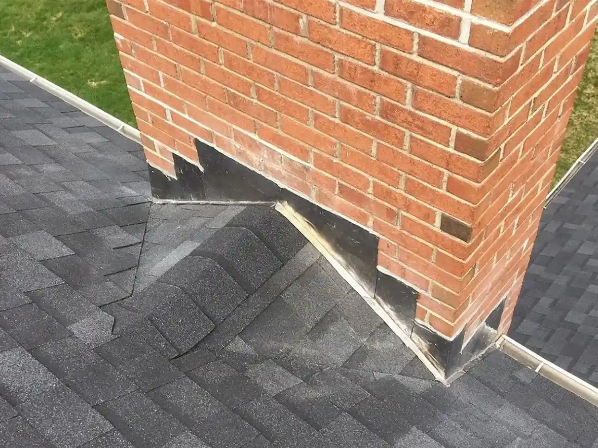 Close-up of a brick chimney on a shingled roof, clearly showing step flashing installed along the seams—a great example for any roof flashing guide.