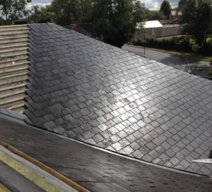 Newly installed slate roof tile on a house, with part of the roof still under construction and exposed wooden battens visible.