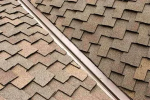 Close-up view of a roof with patterned brown asphalt shingles, highlighting the metal valley where two slopes meet—a key example shown in any roof flashing guide.
