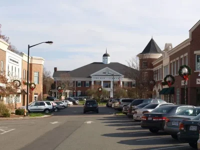 A small town center with parked cars lining both sides of the street, brick buildings with holiday wreaths, and a town hall building in the background—perfect scenery for a trusted roofing company NC to serve the charming local community.
