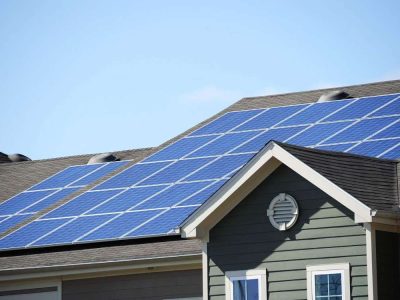 Rooftop with multiple blue solar panels installed on a residential house under a clear blue sky, showcasing modern solar roofing options.